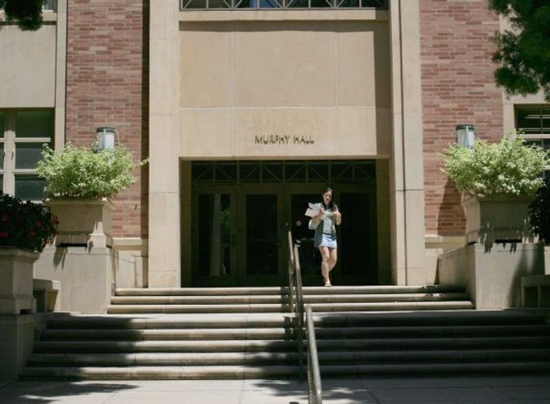 A woman walks out of Murphy Hall holding a folder of papers